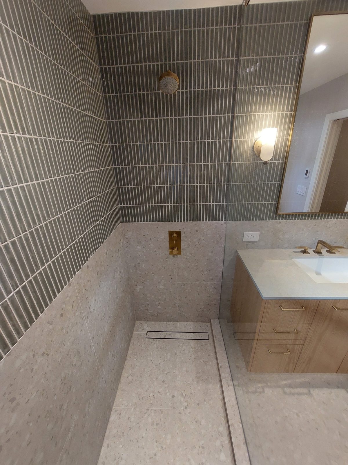 Shower with green kit-kat tile, terrazzo walls and brushed brass fixtures