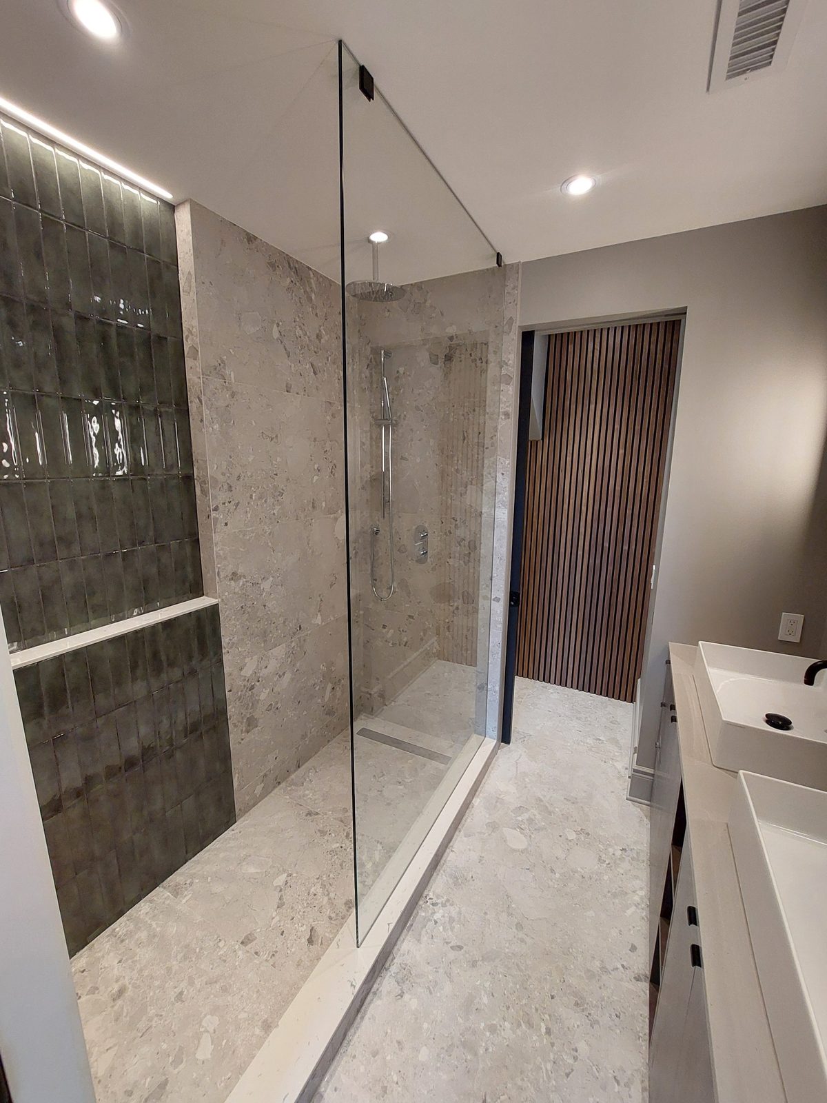 Glass walk-in shower with terrazzo tile, glossy green accents and a timber slat feature wall